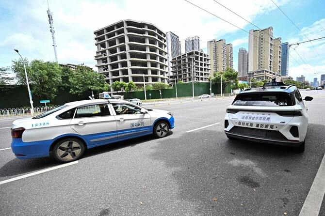 上：中国湖北省武漢市の路上で、タクシーの横を走行するロボットタクシー。(AFP＝時事）