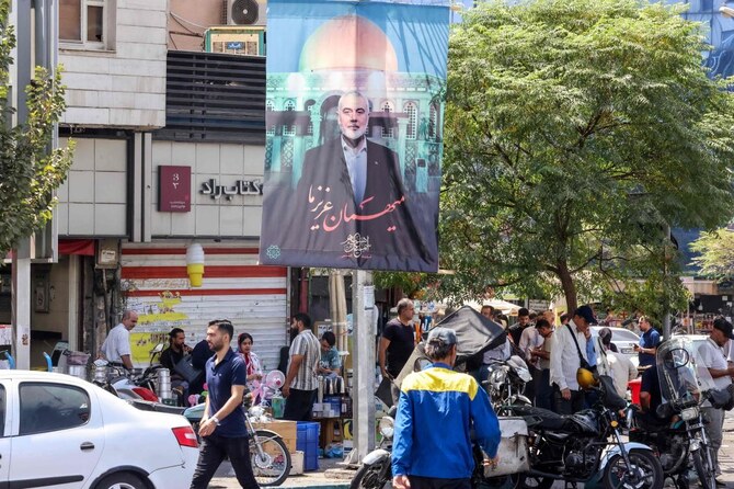 2024年8月20日、テヘランで、イラン滞在中の攻撃で死亡したハマスの故イスマイル・ハニヤ政治指導者の写真をあしらった横断幕の前を通り過ぎる人々。(AFP=時事)
