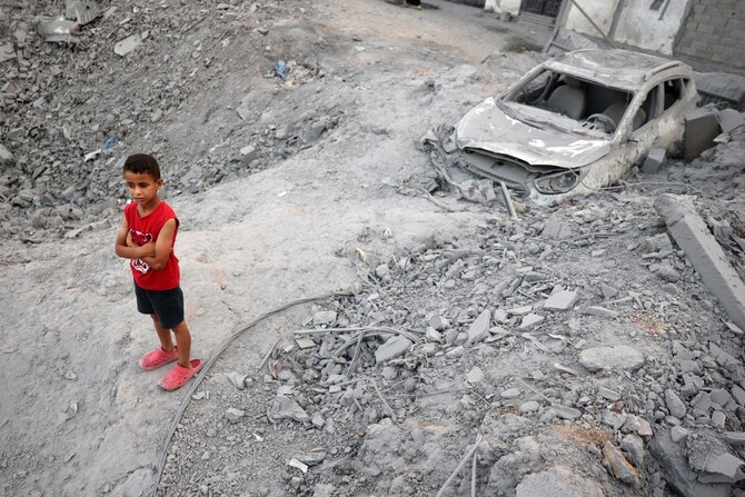 ガザ地区中央部のヌセイラット難民キャンプで、イスラエル軍の爆撃で平地になった直後、がれきの中に埋もれた車の近くに立つパレスチナ人の少年(AFP=時事)