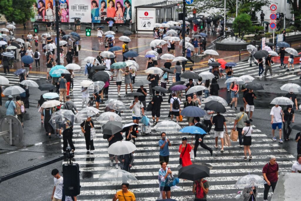 16日、東京都心の渋谷交差点を傘をさして雨をしのぐ歩行者。(AFP＝時事）