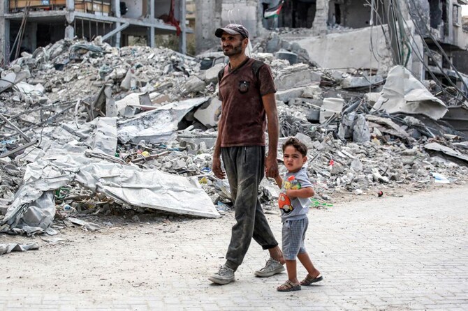 2024年9月16日、イスラエルとハマスの間でパレスチナ自治区で戦闘が続くなか、ガザ地区南部のハーン・ユーニスで、崩壊した建物の瓦礫を子供と歩く男性。(ファイル/AFP)
