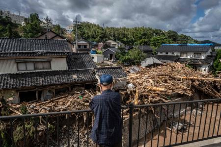 石川県輪島市で大雨が降った後、洪水で流されたがれきが塚田川沿いの家屋に積み上げられている様子を見守る男性。(AFP)