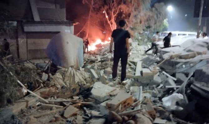 2024年10月8日、シリアの首都ダマスカス西部郊外にあるAl-Mazzehの住宅ビルに対するイスラエル空軍の空爆とされる現場で、損傷した車両のそばに人々が集まっている。(AFP)