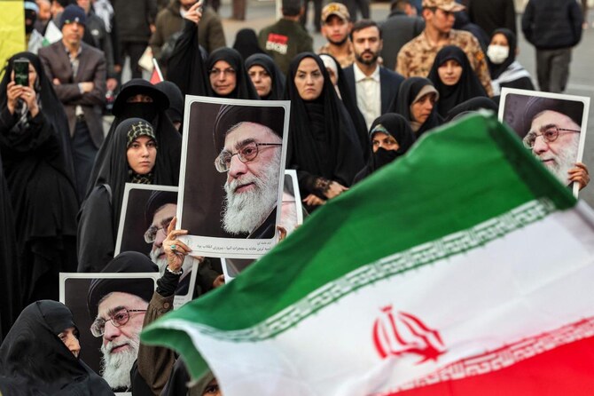 テヘランでの反イスラエル集会で、イランの最高指導者アヤトラ・アリ・ハメネイ師の写真を掲げる女性デモ参加者の前にイラン国旗が翻る。（ファイル/AFP）