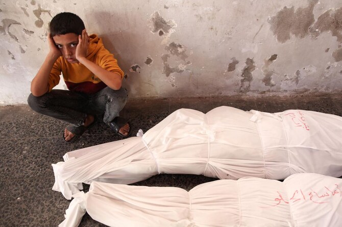イスラエルの攻撃で死亡した人々の覆われた遺体の横に座るパレスチナ人の子供。（AFP）