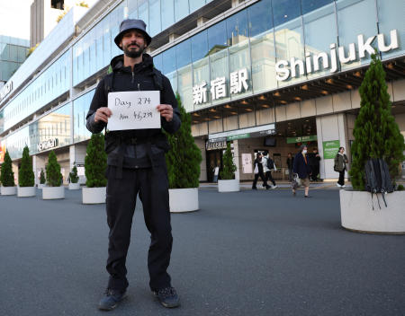 カイロから東京まで陸路で旅した30歳のエジプト人、オマル・ノク氏は、東京・新宿駅前にて、これまでに陸路で旅した日数と距離を記した看板を手に持つ。(ロイター)