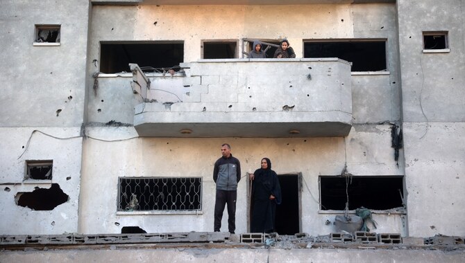 12月1日、ガザ地区中央部のヌセイラットで、イスラエルの空爆で破壊された建物の前にある破損したアパートのバルコニーに立つパレスチナ人（AFP＝時事）
