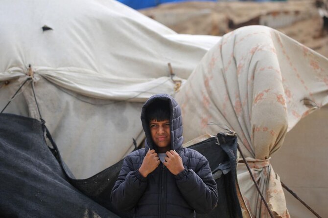 2024年12月20日、イスラエルとハマスの戦争が続く中、ガザ地区中部のヌセイラット難民近くの海岸にある国内避難民キャンプで、風に吹かれながら頭を覆うパレスチナの少年。(AFP＝時事）