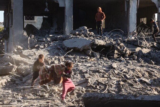 2025年1月3日、イスラエルとハマスとの戦いが続く中、ガザ地区中央部のアル・マガジ難民キャンプで、イスラエル軍の空爆の余波を受け、破壊された中で毛布を拾い集めるパレスチナの子どもたち。(AFP=時事)