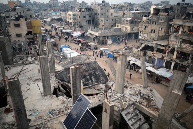 ガザ地区南部のハーン・ユーニスで、イスラエル軍の空爆で破壊された建物の瓦礫の中、商品を売る露店を通り過ぎる人々。(AFP＝時事）