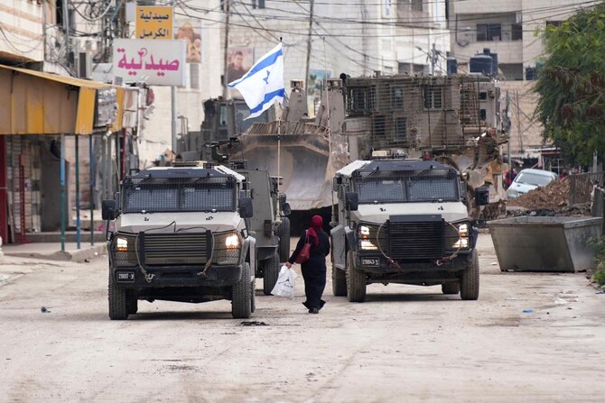 2025年1月22日、ヨルダン川西岸地区ジェニンで、軍事作戦中のイスラエル軍車両の横を通り過ぎるパレスチナ人女性(AFP=時事)。