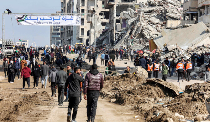 2025年1月26日、イスラエルに封鎖されたガザ地区南部のネツァリム回廊からガザ市へ渡るため、ガザの海岸沿いのアル・ラシッド通り沿いの倒壊した建物の瓦礫のそばで、人々を歓迎する横断幕のそばに集まる人々。(AFP=時事)