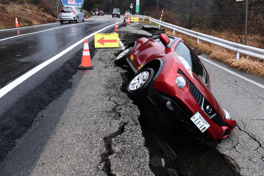 2024年1月6日、元日に能登地方を襲ったマグニチュード7.5の大地震の後、石川県穴水町で、新しく舗装された道路を通行する車（左）と、古い舗装にはまったままの車（右）。(AFP＝時事)