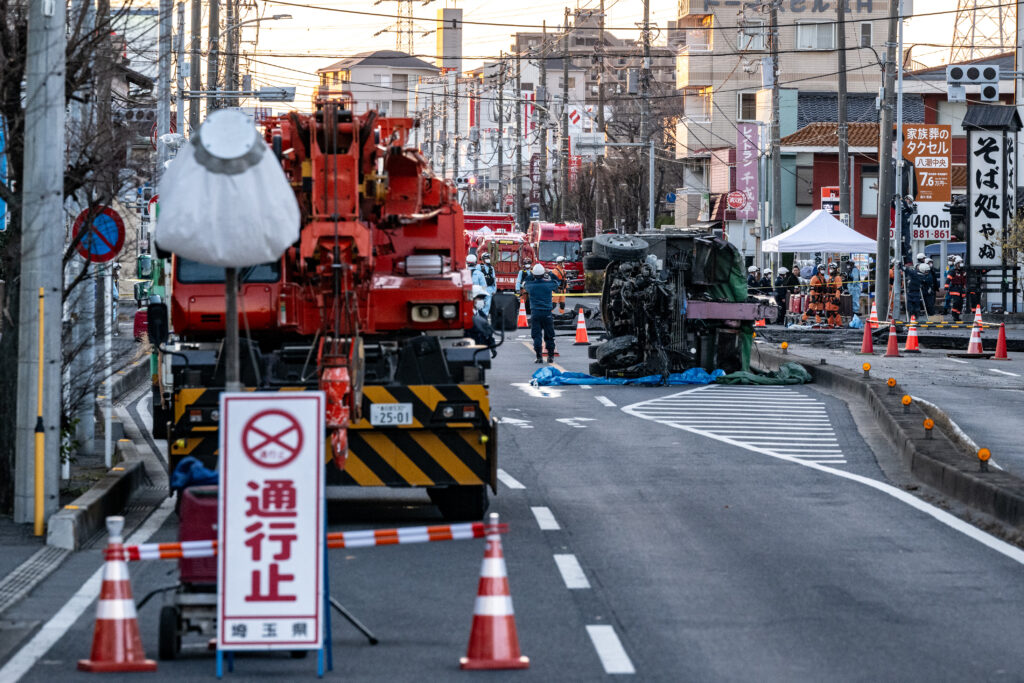 30日、埼玉県八潮市の県道交差点で、陥没穴から引き揚げられたトラックの一部が横倒しになり、運転手の救出作業が続けられている。(AFP=時事)