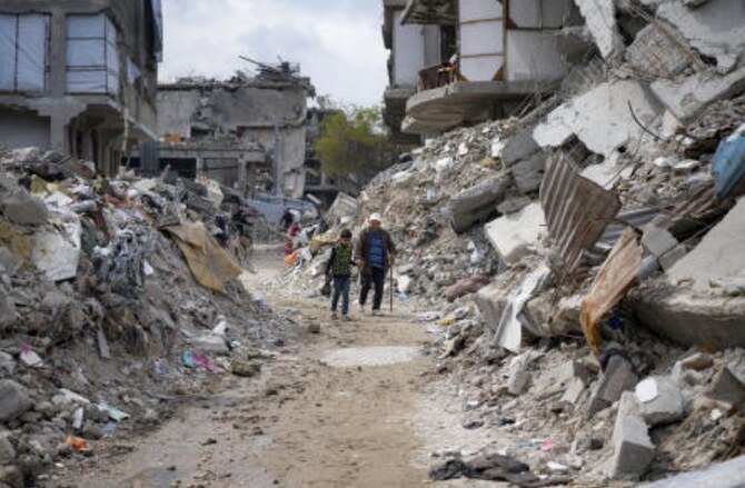 2025年2月19日、ガザ地区北部のジャバリヤで、イスラエル軍のハマスに対する空爆と地上攻撃によって破壊された家屋の瓦礫の中を歩く人々。(AP)