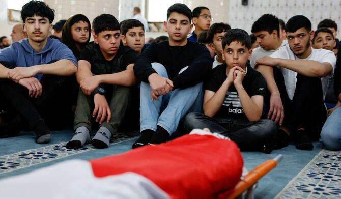 2025年4月7日、イスラエル占領下のヨルダン川西岸地区ラマッラー近郊で、トゥルムスアヤ村でイスラエル軍に殺害されたパレスチナ系米国人の少年オマル・モハマド・ラベアくん(14)の葬儀の際、遺体を囲んで追悼する若者たち。(REUTERS)
