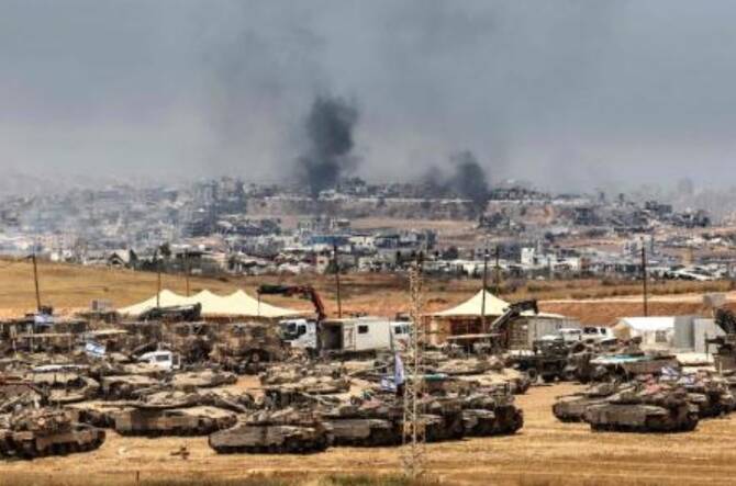2025年5月17日、イスラエル軍の砲撃で破壊されたガザの建物に煙が立ち込める中、イスラエル軍の戦車とブルドーザーが配備されている。(AFP=時事)