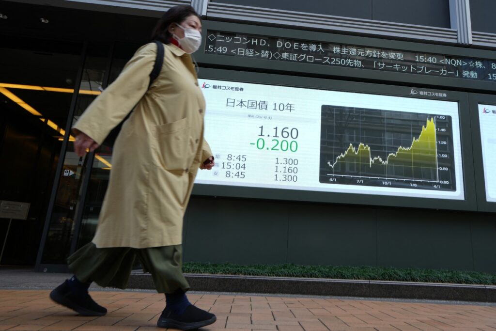 東京債券市場の長期金利を示す電光掲示板の前を通り過ぎる女性(2025年4月4日、東京)。(AFP=時事)