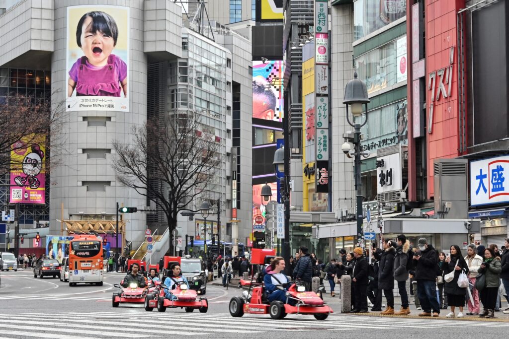 2024年2月6日に撮影されたこの写真では、東京・渋谷で、観光客が「ゴーカート」(中央)に乗って通り過ぎる中、歩行者(右)が道路を横断するのを待っている。新型コロナウイルスの感染制限が解除されて以来、観光客が記録的な人数に急増し、観光客に人気のアクティビティとしてブームとなっている。(AFP)