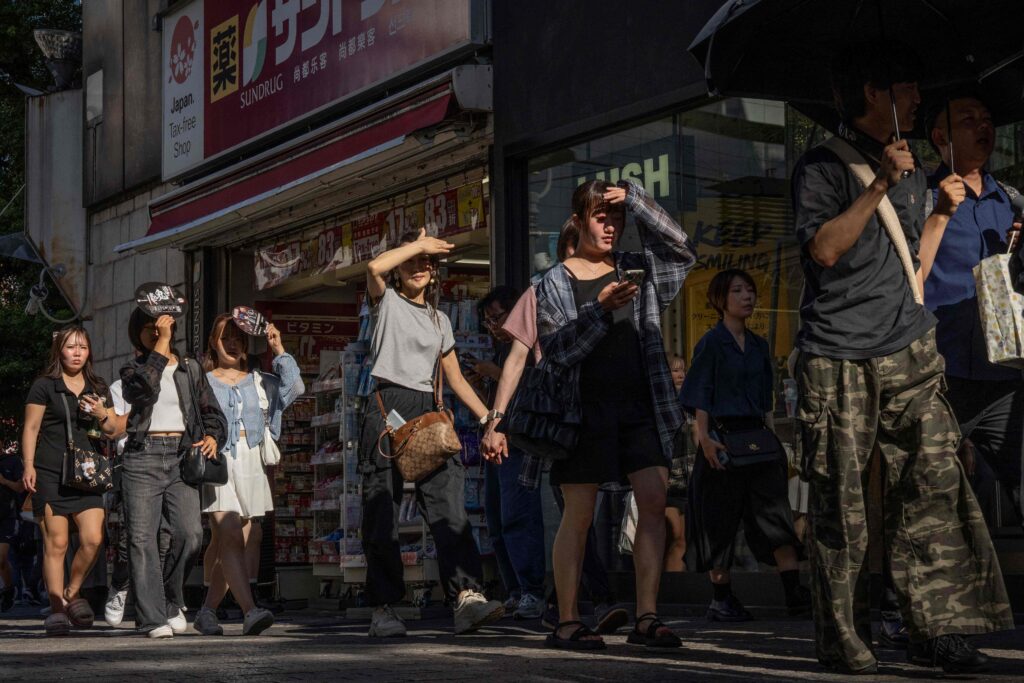 2025年7月26日、東京の暑い日、通りを歩きながら日差しを遮る人々。(AFP=時事)