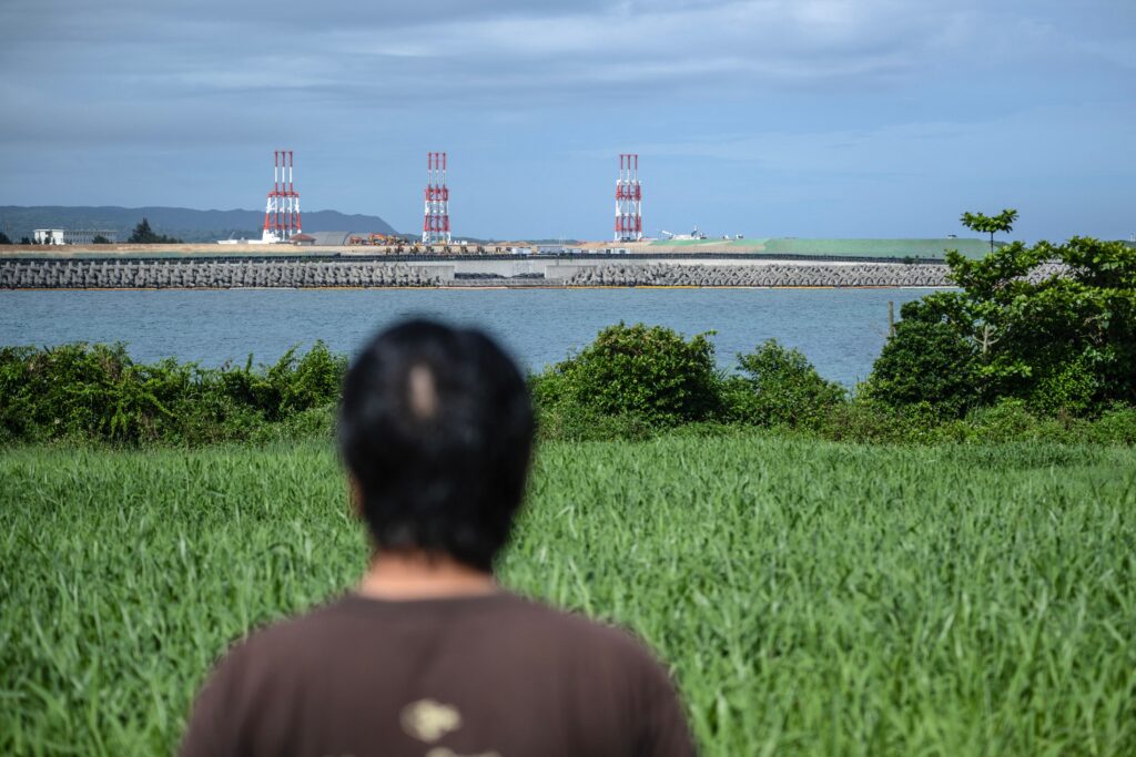 沖縄県名護市の自宅近くの米軍辺野古新基地建設現場を見つめる、1974年に母親が米海兵隊員に殺害された当時高校生だった金城武正さん（2025年6月8日撮影）。(AFP＝時事)