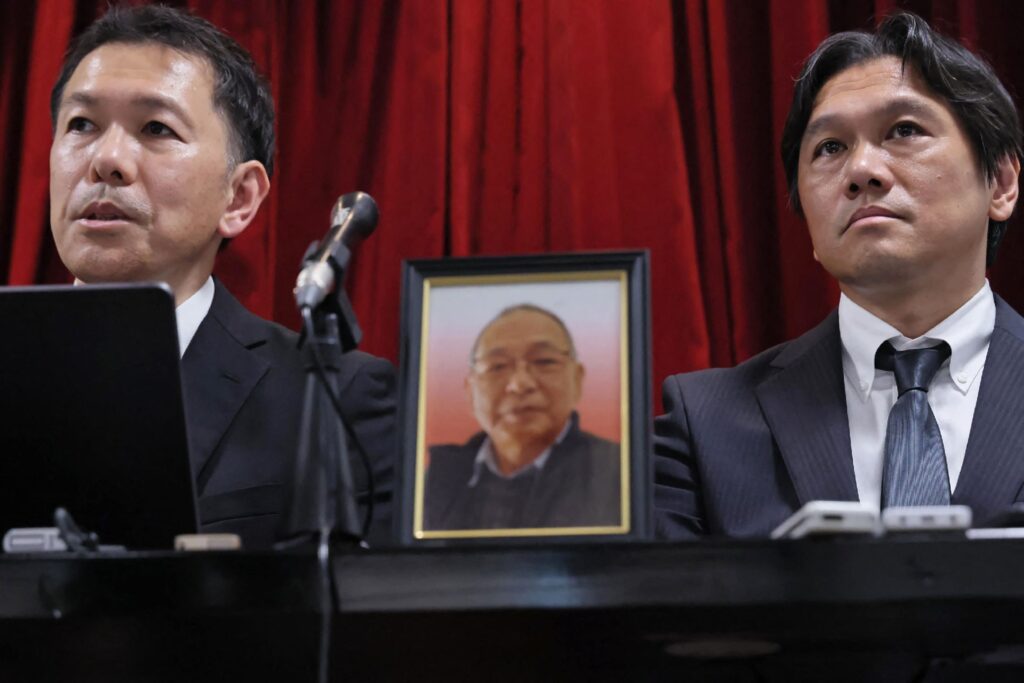 2025年8月25日相嶋氏の墓前で警察と検察が違法な勾留を謝罪した後、記者会見する息子ら=横浜市(AFP=時事)、機密機器不正輸出の濡れ衣を着せられ、長期勾留の末に死亡した故相嶋静夫氏(C)の遺影。