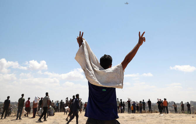 2025年8月5日、イスラエルに包囲されたパレスチナ領土上空で、人道支援物資を積んだ飛行機がガザ地区中央部のヌセイラート上空を飛行する中、男性が反応を示す。（AFP）