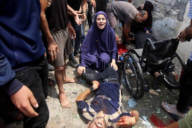 イスラエルの空爆後、パレスチナ人の遺体に触れながら反応する女性（ガザ市）。(ロイター）