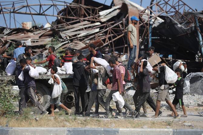 米国とイスラエルが支援するガザ人道基金(GHF)がガザ地区中央部で運営する食料配給所から戻る際、バッグを持つパレスチナ人。(AFP)
