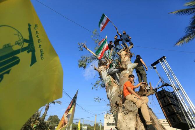 2025年6月25日、イスラエルとイランの停戦を祝うため、ベイルート南郊のイラン大使館前で行われた集会で、木の幹に登りながらイランの国旗を振るレバノンのヒズボラ支持者たち。(AFP=時事)